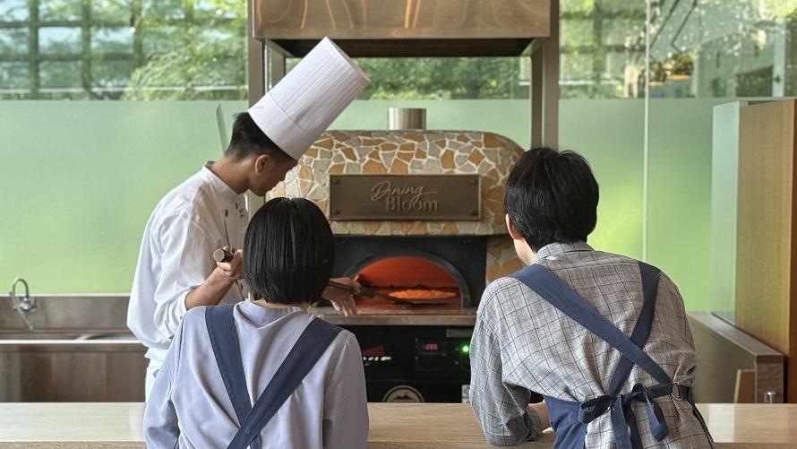 ピザ窯の前でシェフが焼き上げるピザを見つめるカップル