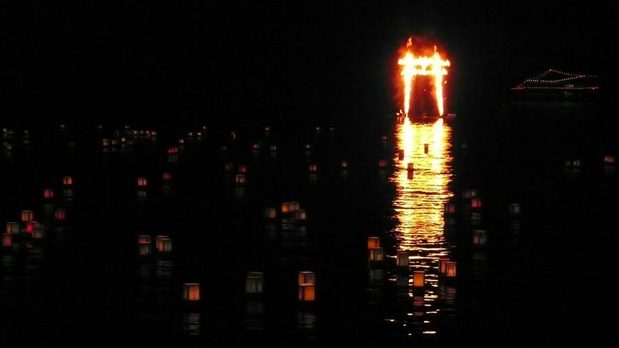 湖面に写る火に燃える鳥居と流し灯篭
