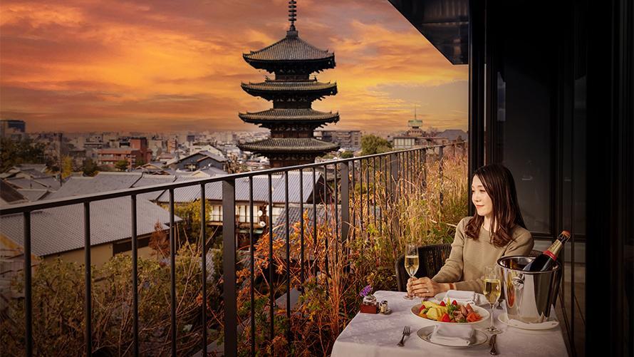 客室パノラミックスイートのテラスで、夕焼けを眺めながらシャンパンとオードブルを楽しむ女性。