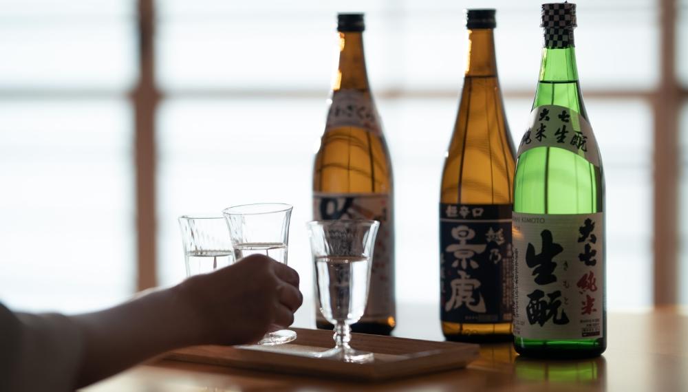 日本酒の瓶が３本並び、利き酒用のグラスに日本酒が注がれている様子。