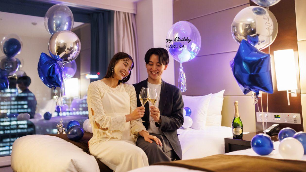 バルーンで飾られたお部屋で乾杯する男女。バルーンにはハッピーバースデーのメッセージ入り。