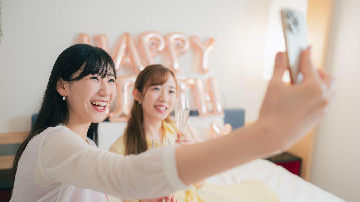 ハッピーバースデーのバルーンを背景にスパークリングワインを持って撮影する女性2人