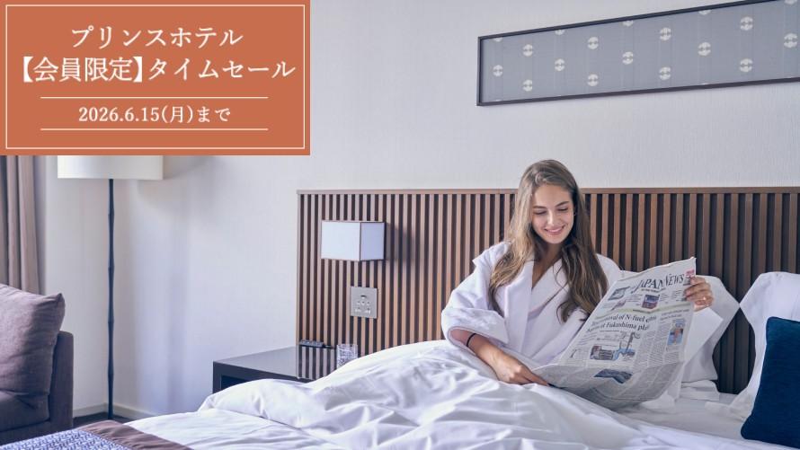 ザ・プリンス さくらタワー東京の客室のベッドで、外国人女性客が新聞を読んでいる。