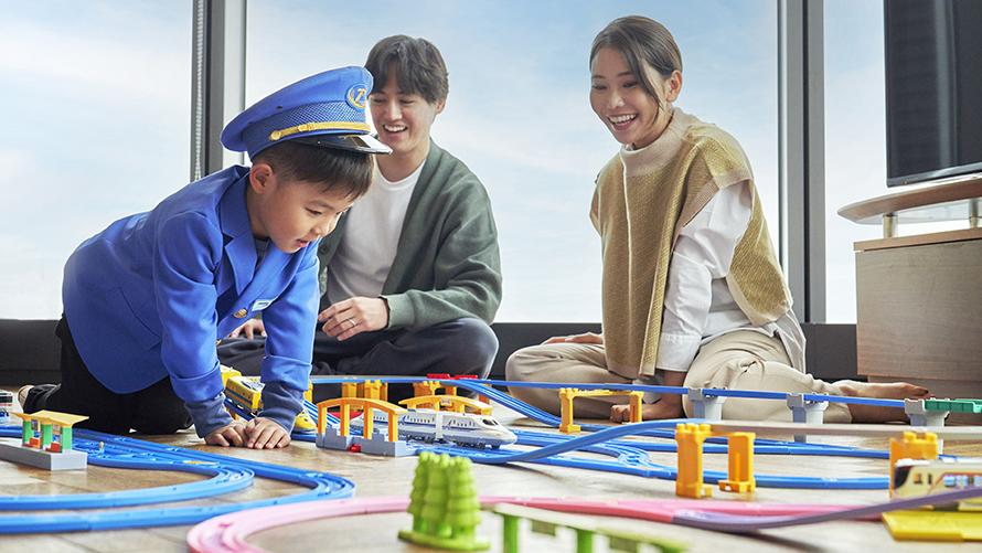 プラレール鉄道の制服を着てプラレールで遊ぶ男の子と笑顔で見守る両親