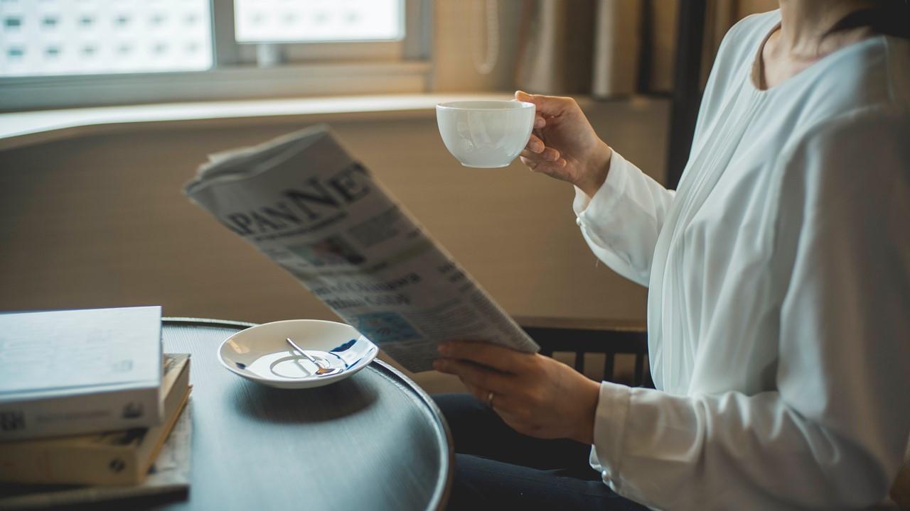 グランドプリンスホテル高輪の客室で、女性が英字新聞片手にコーヒーを飲んでいる。