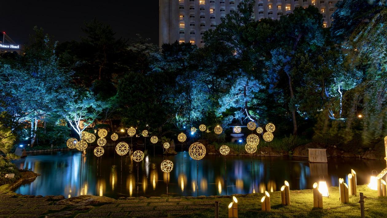 夜の日本庭園で、池に浮かぶ竹まりがライトアップされている。
